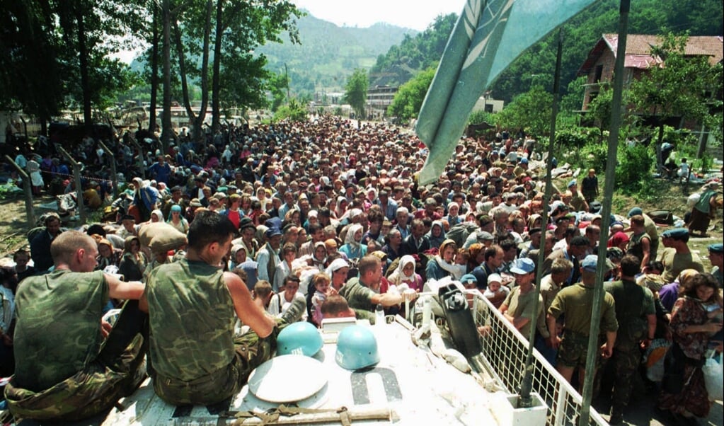 Nederlandse blauwhelmen zitten op donderdag 13 juli 1995 op hun voertuig terwijl moslimvluchtelingen uit Srebrenica zich verzamelen in het dorp Potocari, zo'n vijf kilometer ten noorden van Srebrenica. (beeld hollandse hoogte / ap)
