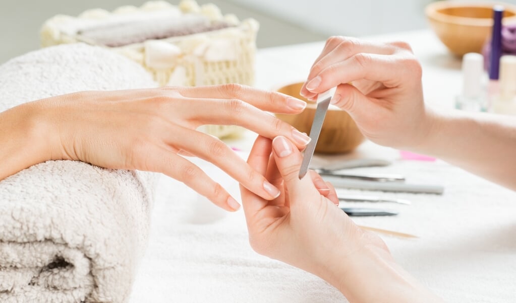 Closeup shot of a woman in a nail salon receiving a manicure by a beautician with nail file. Woman getting nail manicure. Beautician file nails to a customer. Shallow depth of field with focus on nailfile. (beeld Getty Images/iStockphoto)
