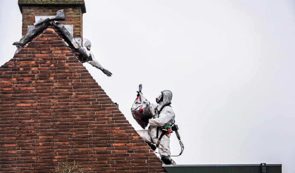 Asbestdeeltjes worden van het dak van een huis verwijderd door mannen in witte pakken. (beeld Raymond Rutting)