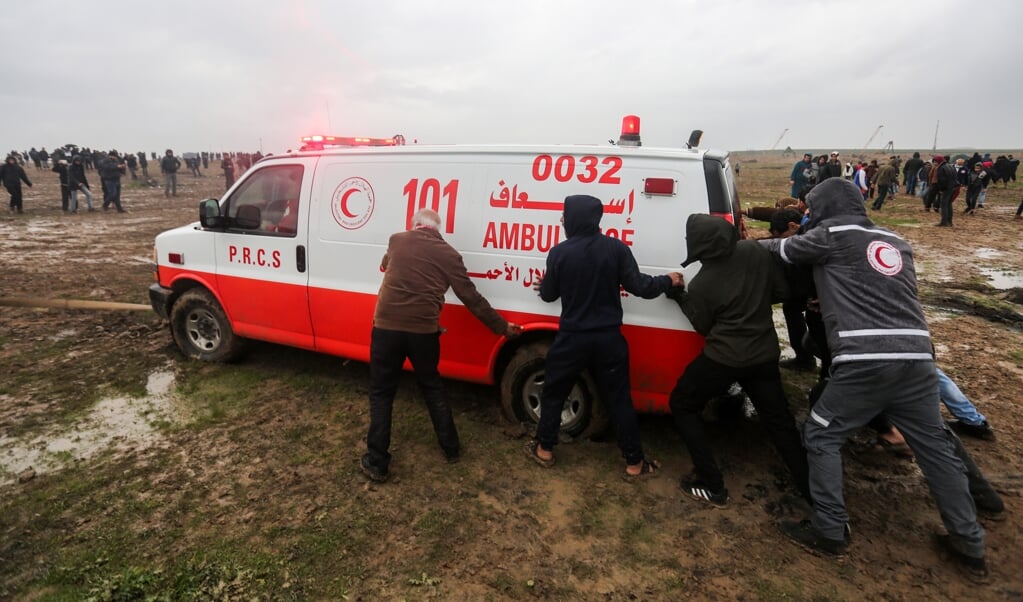Archieffoto uit december 2018: Palestijnse demonstranten duwen een vastgelopen ambulance uit de modder. (beeld afp/Mahmud Hams)