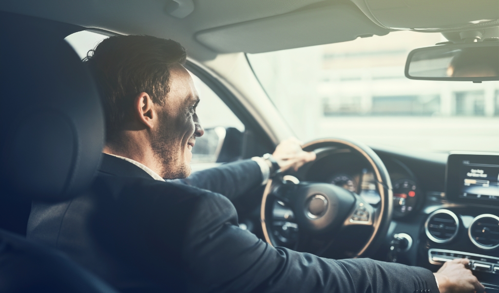 Young businessman smiling and changing stations on his car radio while driving through the city during his morning commute to work (beeld istock)