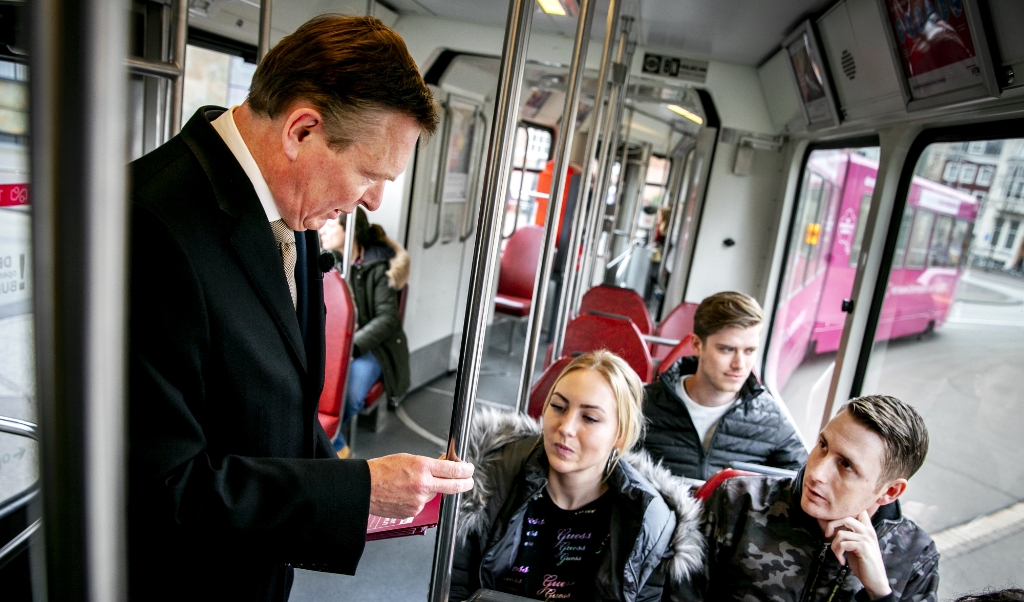 Minister Bruno Bruins van Volksgezondheid deelt in de tram folders uit om de nieuwe donorwet onder de aandacht te brengen. (beeld anp / Remko de Waal)