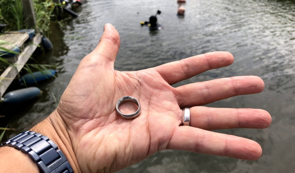 Deze ring werd opgedoken. Op de achtergrond de duiker die de ring gevonden heeft. (beeld Gevonden-verloren)