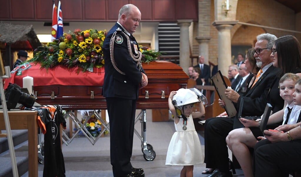 De Australische Charlotte O'Dwyer (1) draagt de brandweerhelm van haar vader Andrew, tijdens zijn begrafenis. (beeld EPA)