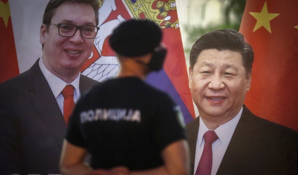 <p>Een agent van de Servische oproerpolitie staat bij een verkiezingsposter in Belgrado, mei dit jaar. Op de poster staan de Servische president Aleksandar Vucic (links) en de Chinese leider Xi Jinping afgebeeld.</p> (beeld afp / Oliver Bunic)