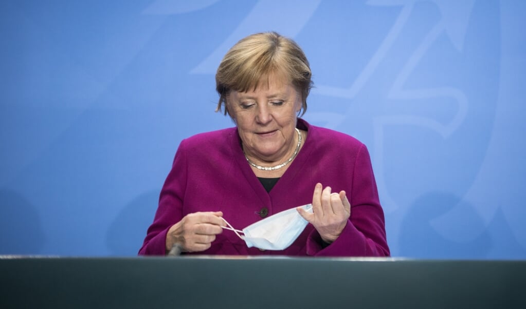 <p>Bondskanselier Merkel doet haar mondkapje af bij het begin van een persconferentie afgelopen week.</p> (beeld AFP / Stefanie Loos)