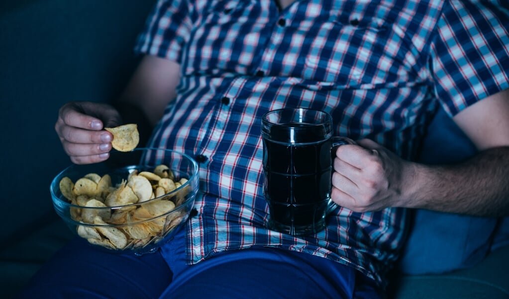 overweight man watching tv with junk food and beer. overeating, sedentary lifestyle, bad habits, food addiction, eating disorders (beeld istock)