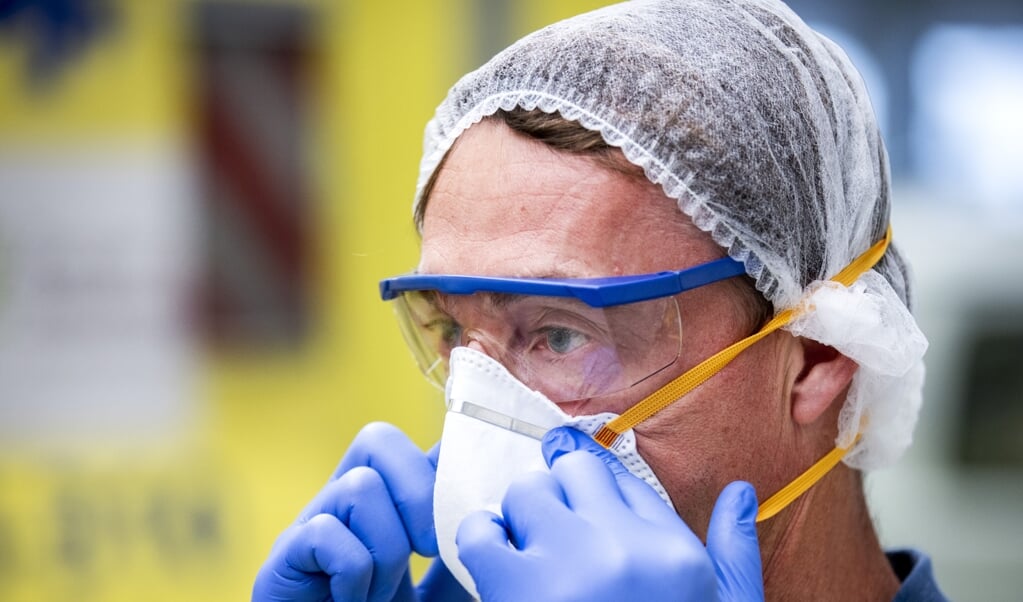 <p>Een ambulancemedewerker trekt beschermende kleding aan in een ambulancepost van het RAV Hollands Midden.</p> (beeld anp / Remko de Waal)