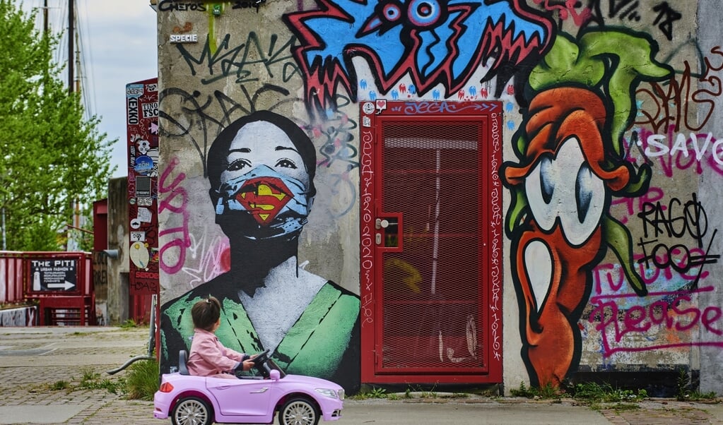 Een meisje kijkt naar graffitikunst van een superverpleegster op het NDSM-plein in Amsterdam. (beeld Nico Garstman)