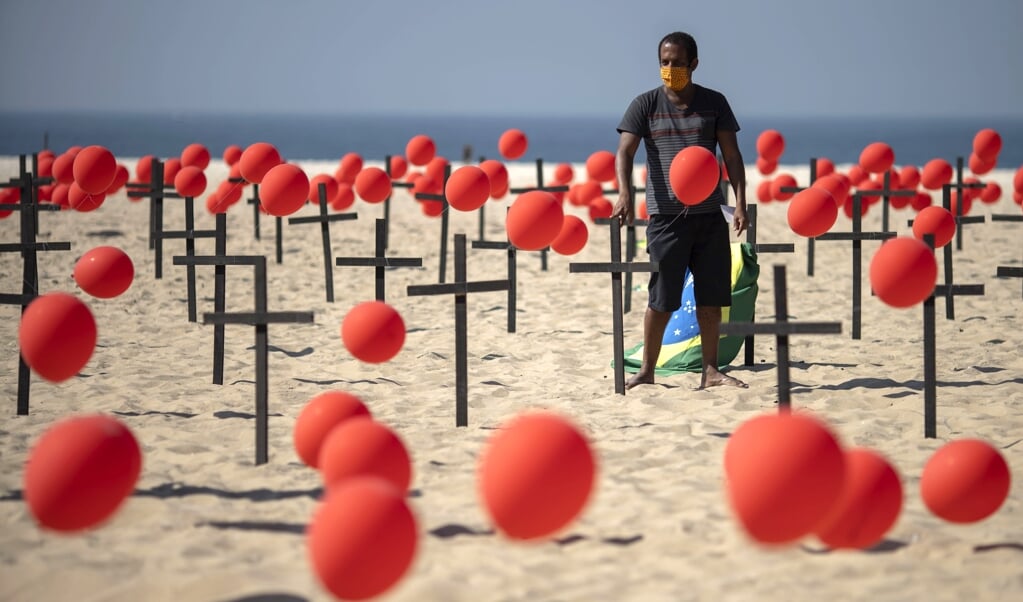 Brazilianen op het strand van Rio de Janeiro brengen met kruizen en ballonnen een eerbetoon aan meer dan honderdduizend coronadoden. (beeld afp / Mauro Pimentel)