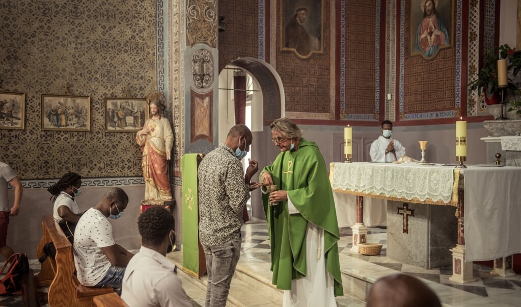 De Nederlandse priester Martin Schneeberger deelt de communie uit aan christelijke vluchtelingen op het Griekse eiland Lesbos. (beeld Mathias Benguigui)
