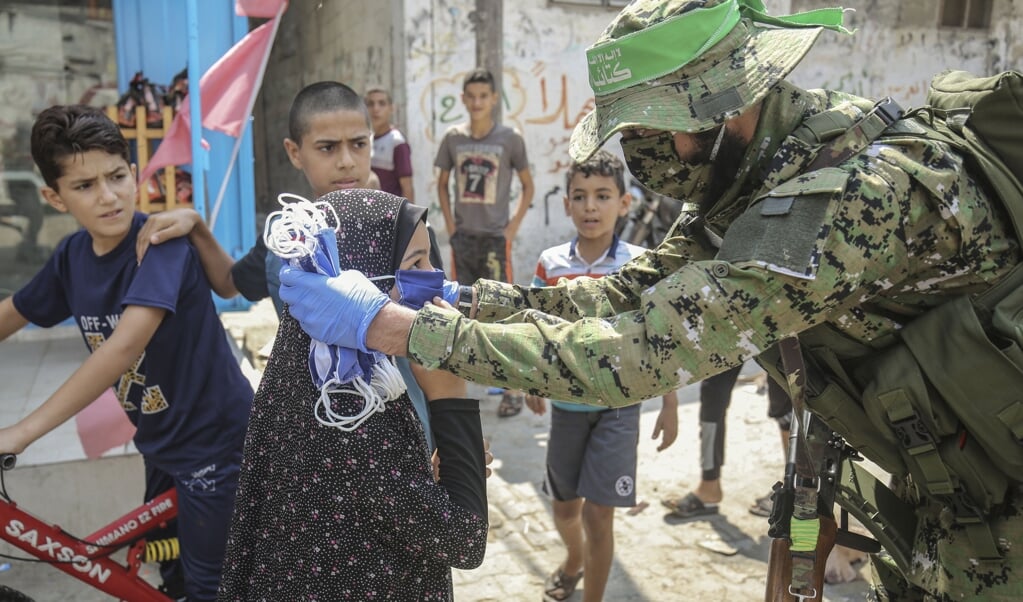<p>Een strijder van een gewapende vleugel van Hamas deelt in de Gazastrook beschermende maskers uit op straat .</p> (beeld afp / Said Khatib )