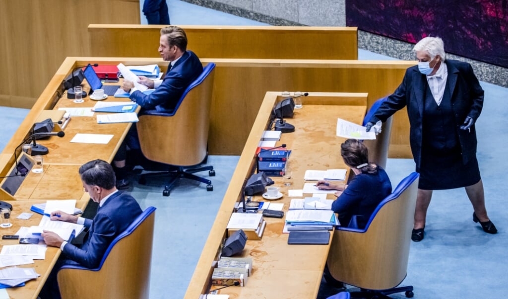 <p>Een Kamerbode draagt een mondkapje tijdens het debat over het coronavirus.</p> (beeld anp / Remko de Waal)