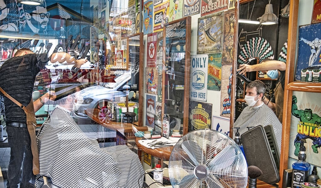 <p>Een barbershop op de Nieuwe Binnenweg in Rotterdam. Zowel de klant als de kapper draagt een mondkapje. Verder heeft de zaak plexiglas, extra ventilatie en wordt er alleen gekapt op afspraak.</p> (beeld Guus Dubbelman)