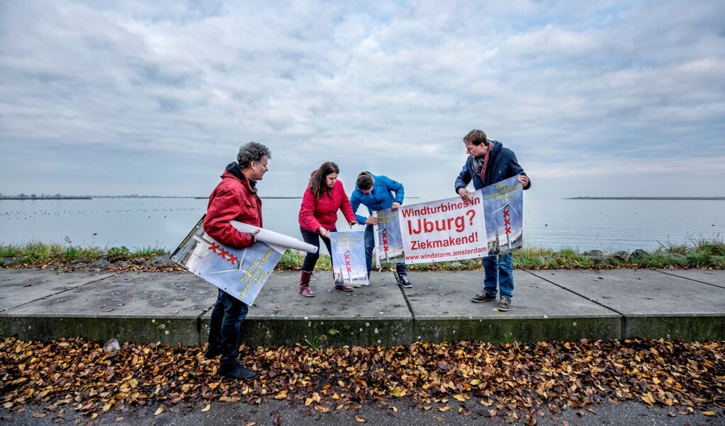 Actievoerders van Windalarm Amsterdam rollen op IJburg hun spandoeken uit bij de plek waar de windmolens moeten komen. (beeld Raymond Rutting)