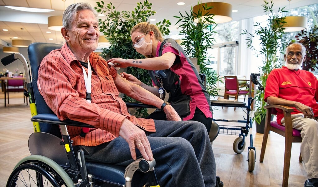 Voormalig psycholoog Bart Uijterlinde (91) ondergaat lachend de prik. De bewoner van een verpleeghuis in Haarlem voelt zich daarna 'kiplekker', zegt hij. Jamiel Ramzam kijkt toe. (beeld Guus Dubbelman)