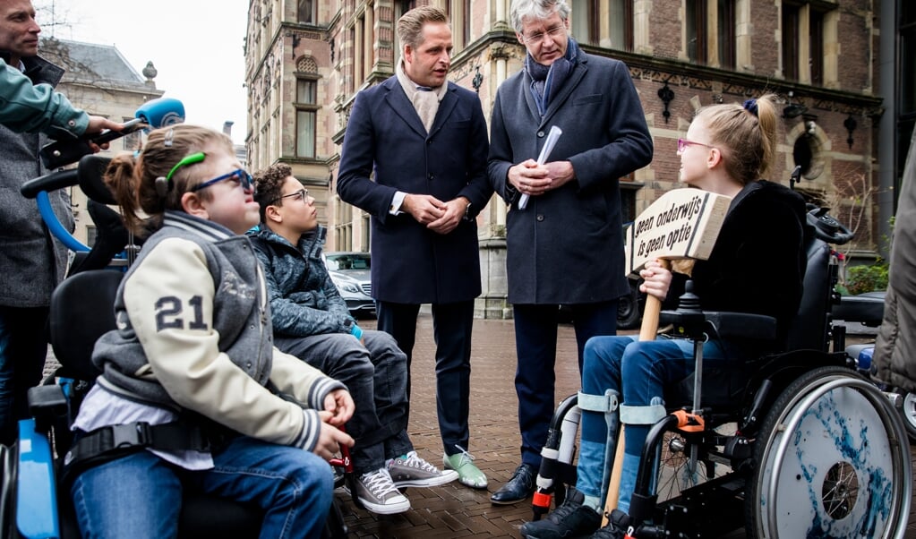 De ministers Hugo de Jonge en Arie Slob kregen begin 2019 van drie kinderen met een beperking een sloophamer cadeau, met als boodschap: sloop de muur tussen zorg en onderwijs. Nog steeds komt inclusief onderwijs maar moeilijk tot stand, schrijven Henk-Willem Laan en Tim Vreugdenhil. (beeld anp / Bart Maat)