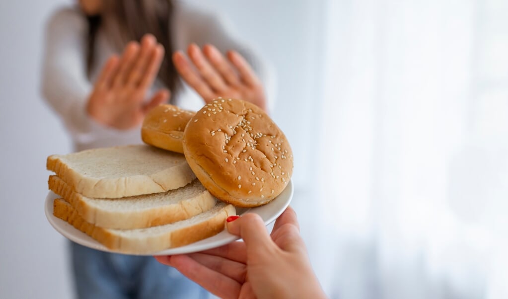 Young woman suffers from a gluten. Gluten intolerant and Gluten free diet concept, Real people. Copy space. Gluten intolerance and diet concept. Woman refuses to eat white bread. Selective focus on bread (Young woman suffers from a gluten. Gluten into (beeld istock)