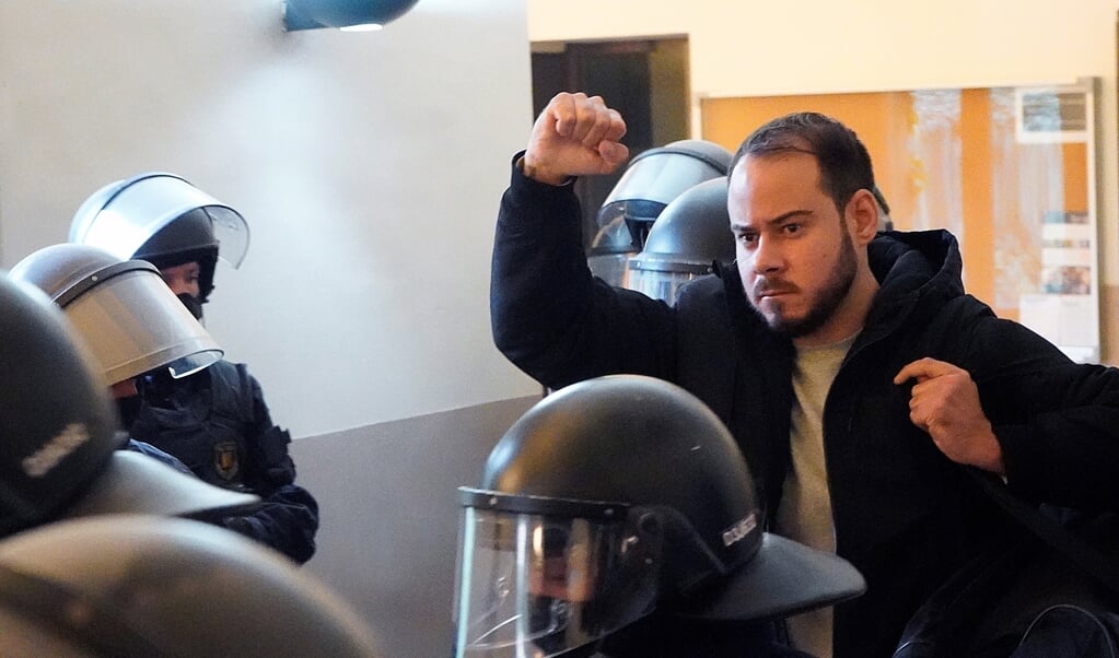 Met opgeheven vuist richt Pablo Hasél zich tot een groepje journalisten, terwijl hij uit het gebouw van de universiteit van Lleida afgevoerd wordt door een dozijn agenten van de oproerpolitie. (beeld epa / Paul de la Calle)