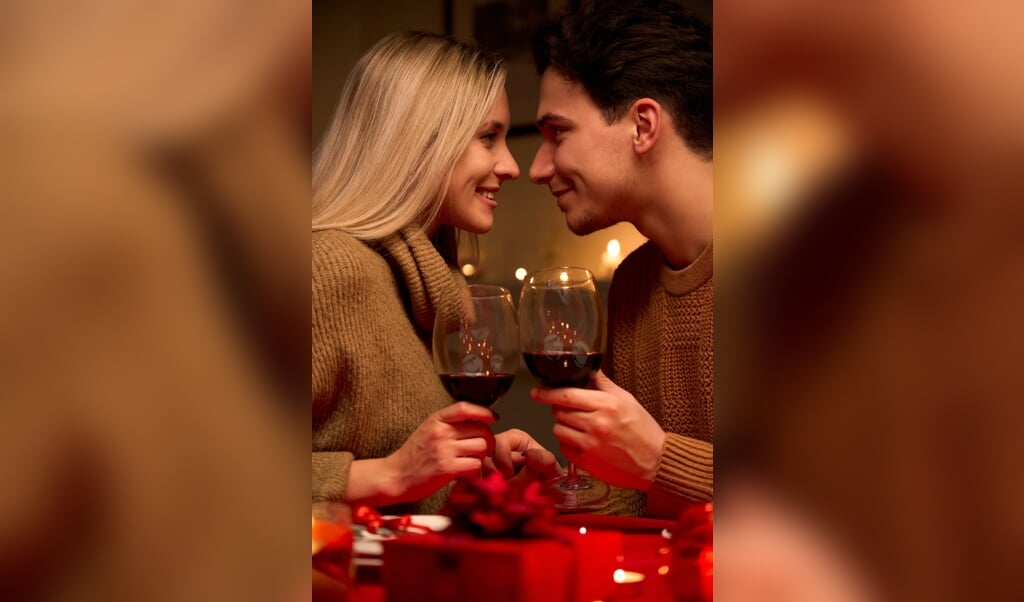 Happy young couple in love bonding, holding glasses, drinking wine, enjoy tender moment together celebrating Valentines day having romantic dinner date with candles sit at home table or in restaurant. (beeld Getty Images/iStockphoto)