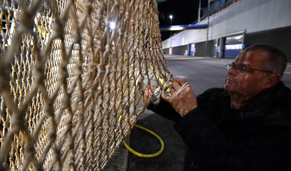 Een Texelse visser repareert een elektrisch pulsnet, nadat hij zijn vangst in de haven van Den Helder heeft gelost. (beeld afp / Emmanuel Dunand)