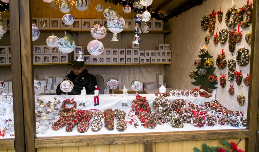 Luxe kerstballen te koop, met tafereeltjes die dezelfde sfeer ademen als de kerstmarkt. Achter de opgetuigde kerstkransjes een verkoper verdiept in zijn smartphone. (Dick Vos)