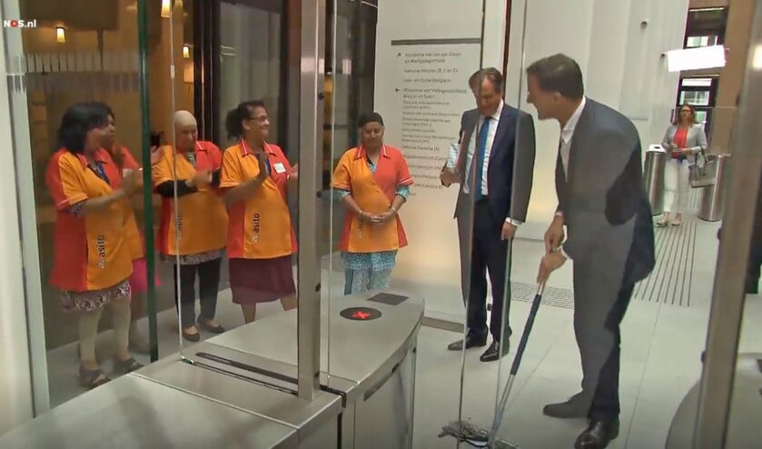 Beeld uit het filmpje van de NOS: Mark Rutte mopt zijn gemorste koffie op, terwijl schoonmakers en D66-fractievoorzitter Alexander Pechtold lachend toekijken. (nd)