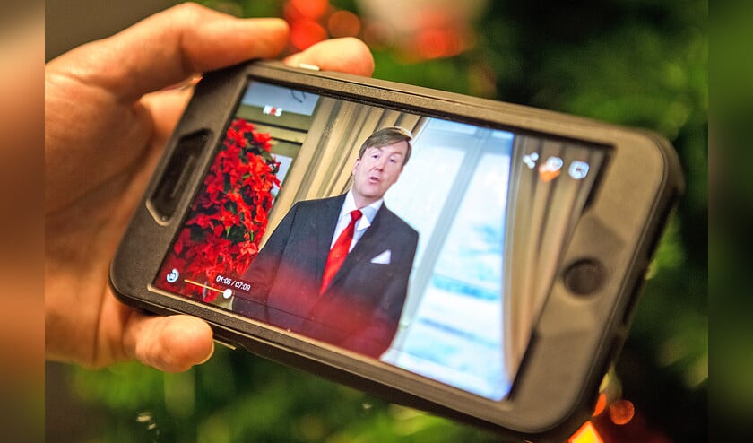 Een belangstellende volgt de kersttoespraak van Koning Willem-Alexander op zijn mobiele telefoon. (anp / Alexander Schippers)