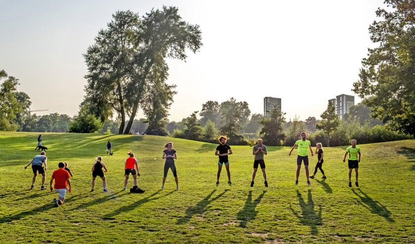 Een bootcampgroep werkt zich in het zweet in het Prins Hendrikpark in ’s-Hertogenbosch, met hondenuitlaters en rustzoekers op de achtergrond. (Raymond Rutting)