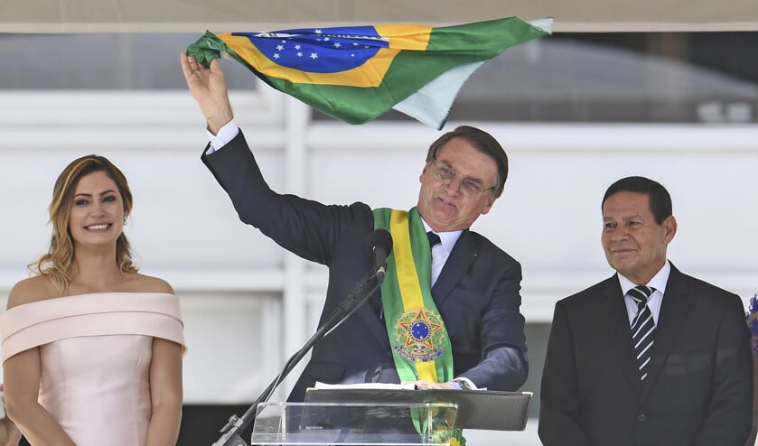 Jair Bolsonaro houdt de Braziliaanse vlag omhoog tijdens de beëdigingsceremonie. Naast hem zijn vrouw Michelle en de nieuwe vicepresident Hamilton Mourao. (afp / Evaristo Sa)