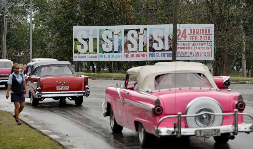 Oude Amerikaanse auto’s rijden langs aanplakbiljetten in Havana waarop de Cubaanse regering haar burgers oproept te stemmen voor een nieuwe grondwet. (afp / Yamil Lage)