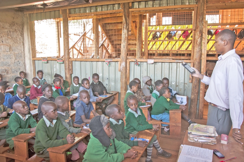 Een schoolmeester geeft op een Bridgeschool in Kangemi (Nairobi) les met een tablet die hem vertelt wat hij moet zeggen en vragen, en wanneer de schooldag begint en is afgelopen. (David Mutua)