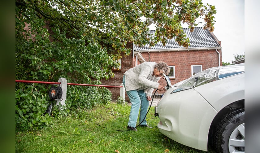 Rika Brik (74) stopt de stekker in een van de elektrische deelauto’s in haar dorp. ‘Laatst vroeg iemand of ik een keer met haar naar de Aldi wilde.’ (Harry Cock)