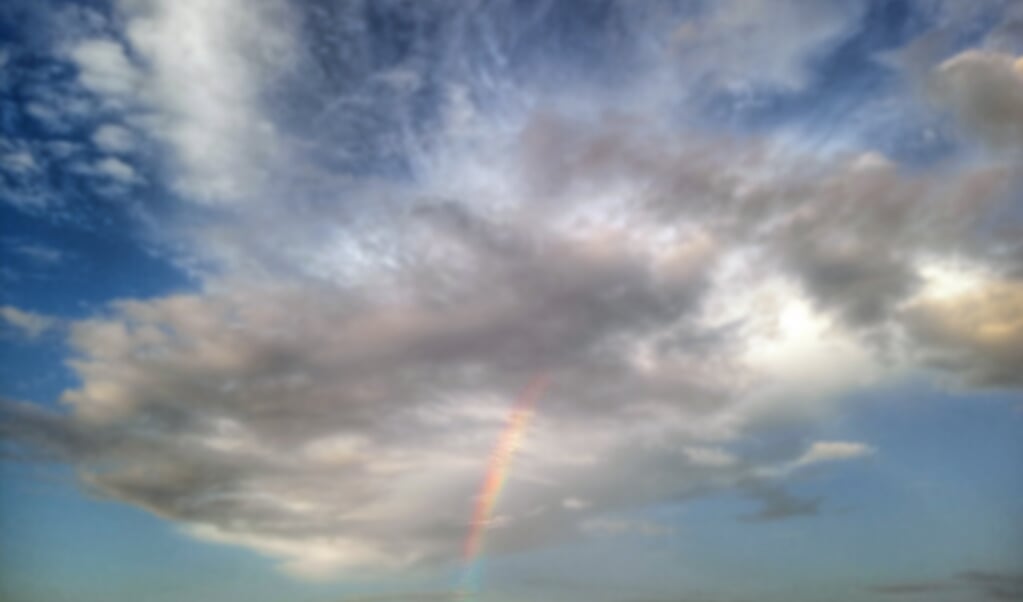Blurry background of rainbow and the storm clouds. Cloud human shape in spiritual imagination, blessing lights. Blue sky clouds background. Copy space for your text design. (beeld istock)